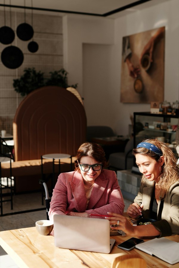Two members creating side by side at a sunlit cafe table